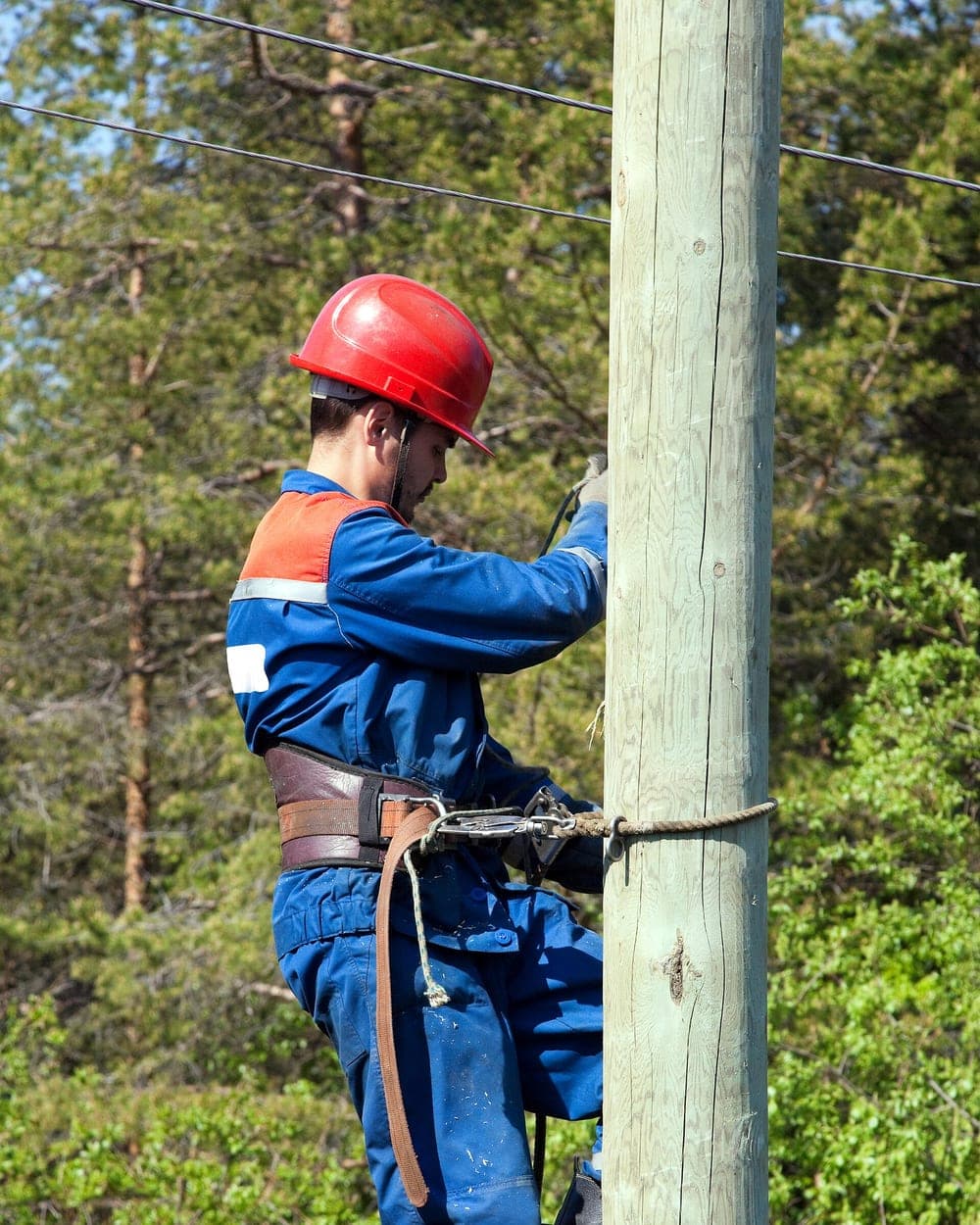 An electrician working at height on a power line, wearing full safety gear